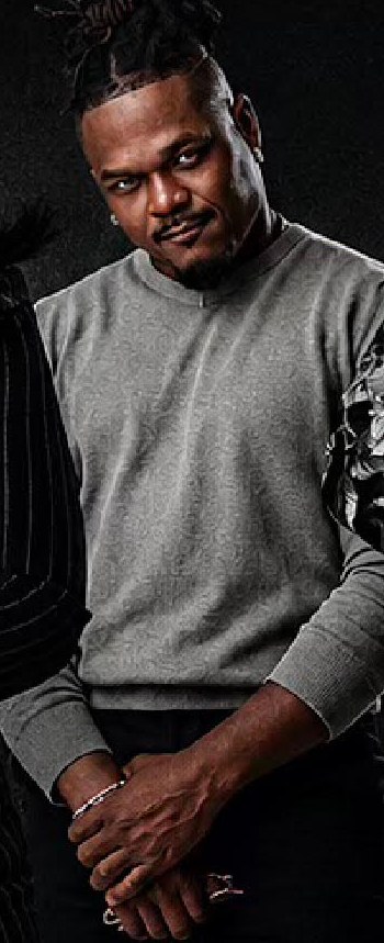 Cast member in a gray sweater, hands clasped
